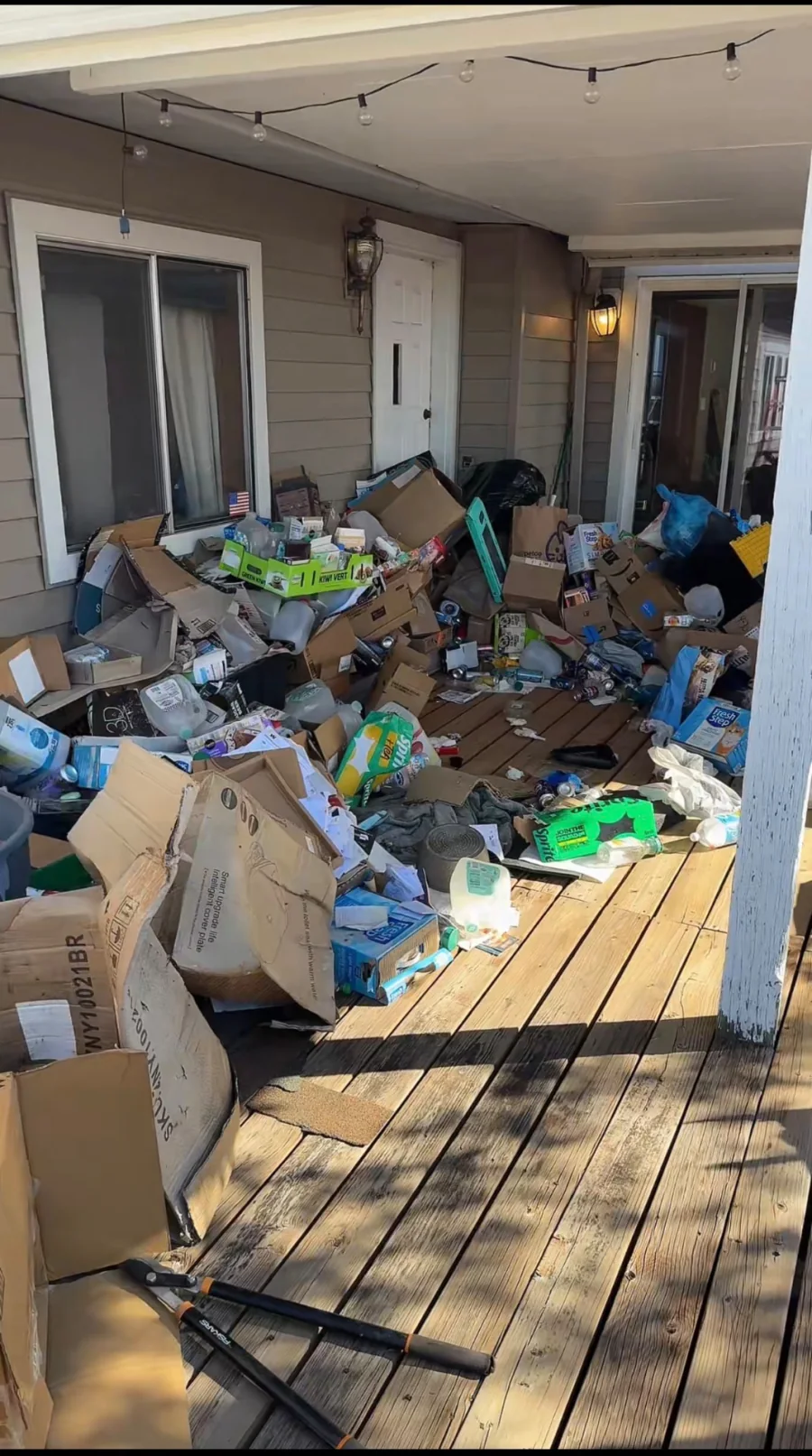 Deck and patio covered with cardboard, bags, household junk, and miscellaneous debris before cleanout